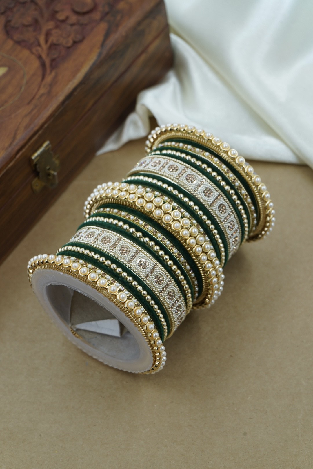 Set of green and gold bangles on a white stand with a wooden box in the background by hitesh bangles