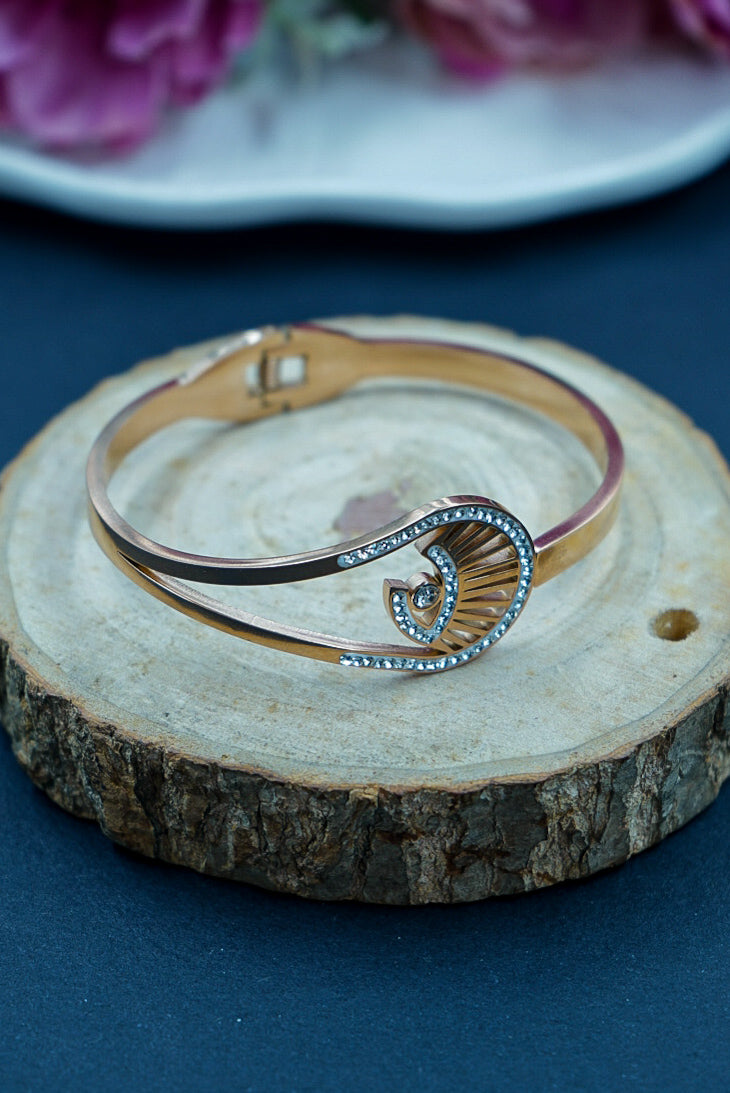 Gold and silver bracelet on a wooden surface with flowers in the background by hitesh bangles