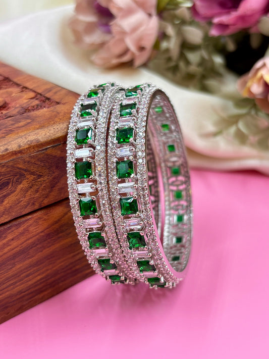 Green gemstone bangles on a pink surface with blurred flowers in the background by hitesh bangles