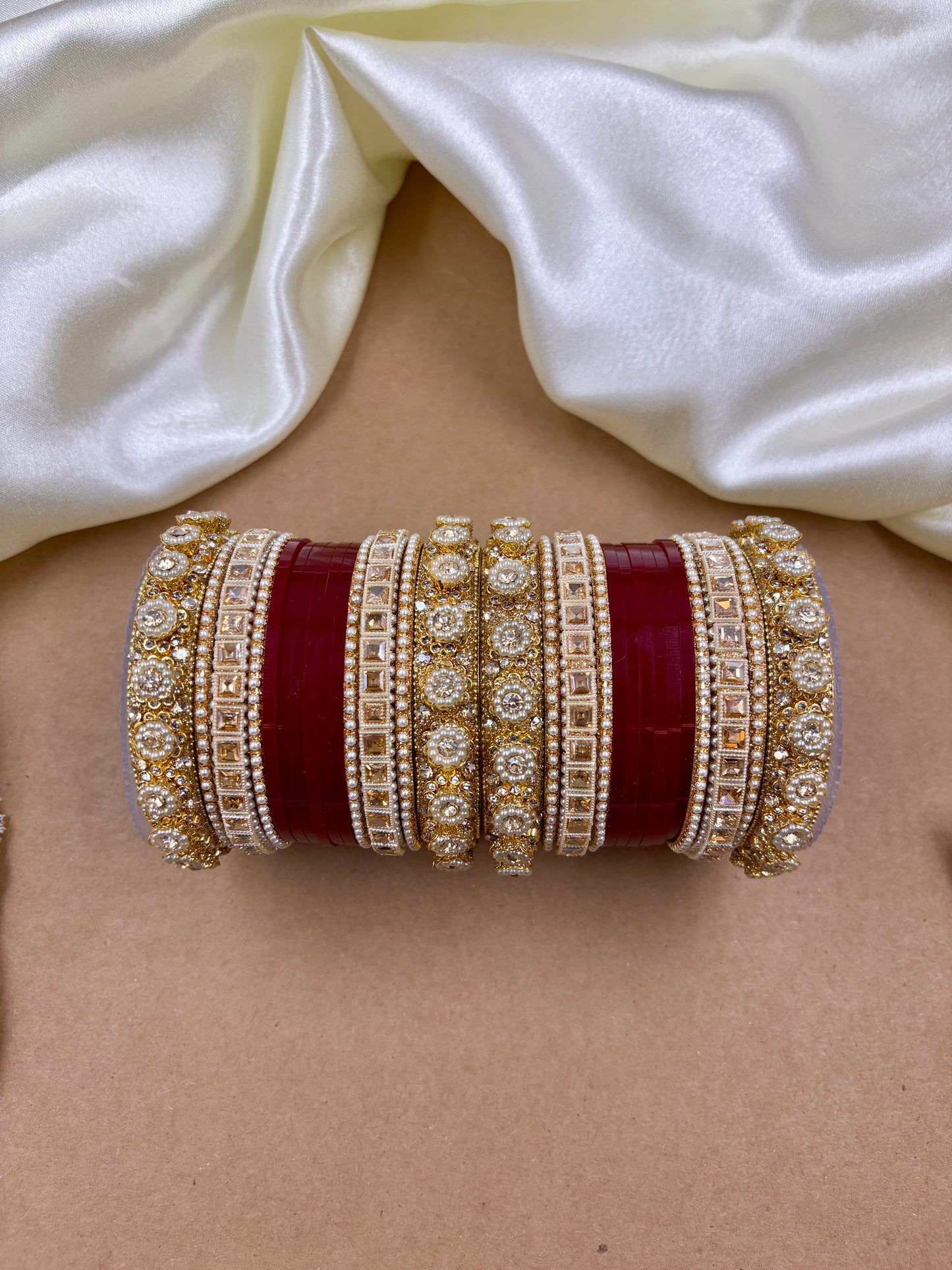 Close-up of a person wearing multiple gold and red bangles on a white fabric background by hitesh bangles
