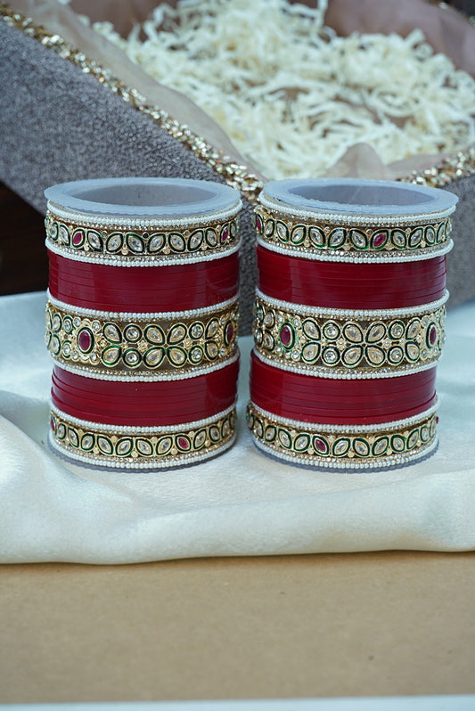 Pair of red and gold bangles on a white surface with a blurred background by hitesh bangles