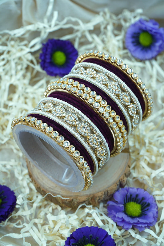 Set of ornate bangles on a wooden slice with purple flowers by hitesh bangles