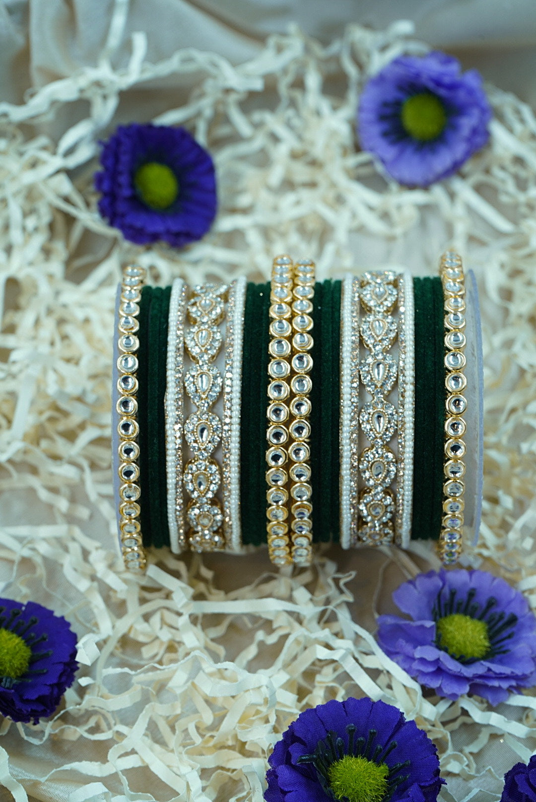 Set of decorative bangles with intricate designs on a white surface with purple flowers by hitesh bangles