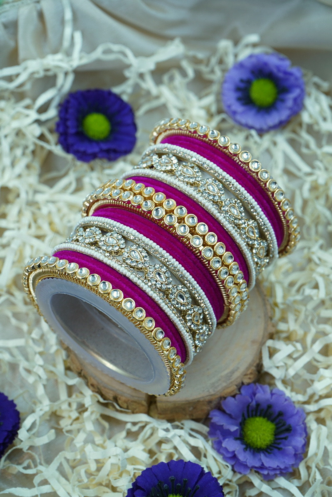 Decorative bangles on a wooden block with purple flowers around by hitesh bangles
