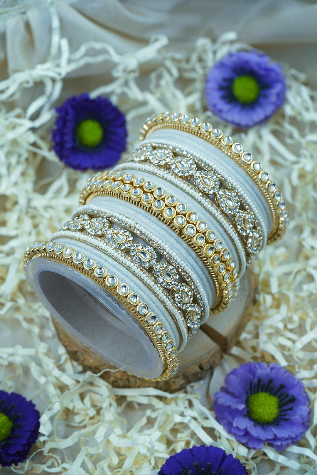 Decorative bangles with intricate designs on a white surface with purple flowers by hitesh bangles