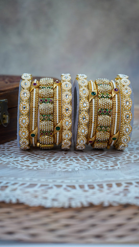 Pair of ornate gold bangles with gemstones on a textured surface by hitesh bangles