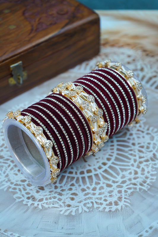 Set of maroon and gold bangles on a white doily with a wooden box in the background by hitesh bangles