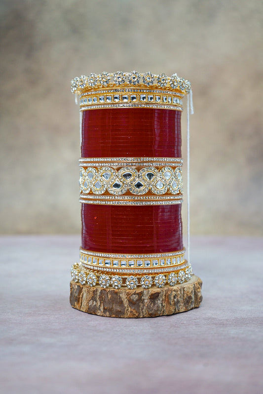 Decorative cylindrical object with red center and gold and silver embellishments on a neutral background by hitesh bangles