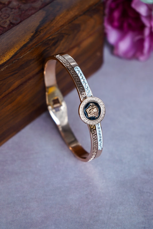 Gold bracelet with a central emblem on a textured surface by hitesh bangles