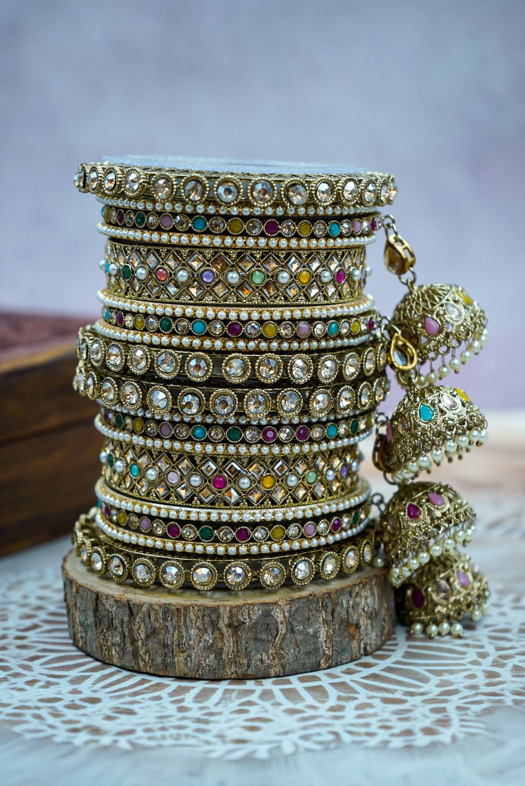 Stack of ornate bangles with colorful stones on a wooden block against a light background by hitesh bangles