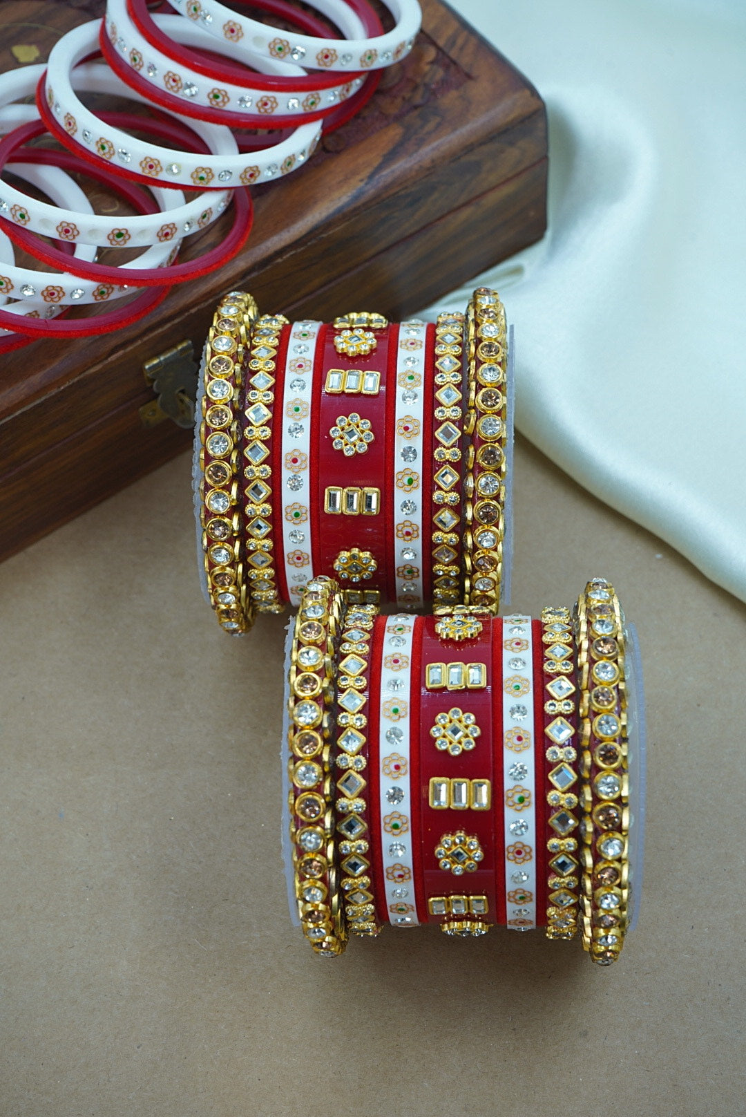 Decorative red and gold bangles on a beige surface with additional bangles in the background by hitesh bangles