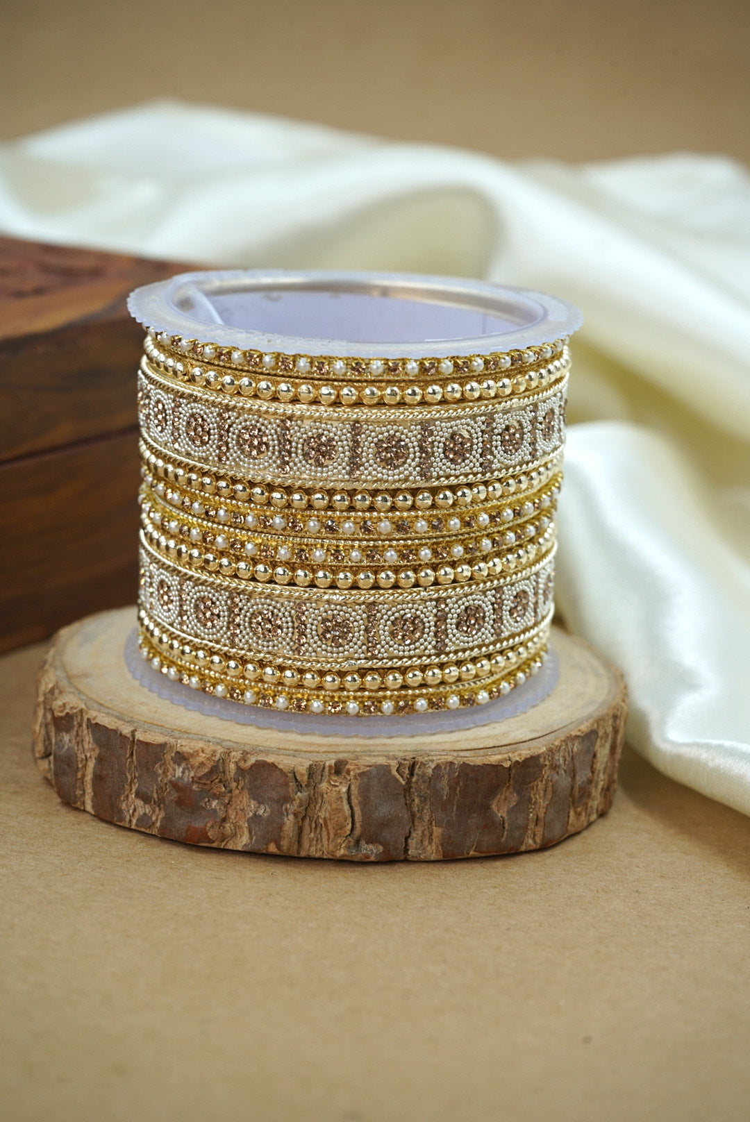Spool of gold bangles on a wooden block with a white fabric background by hitesh bangles