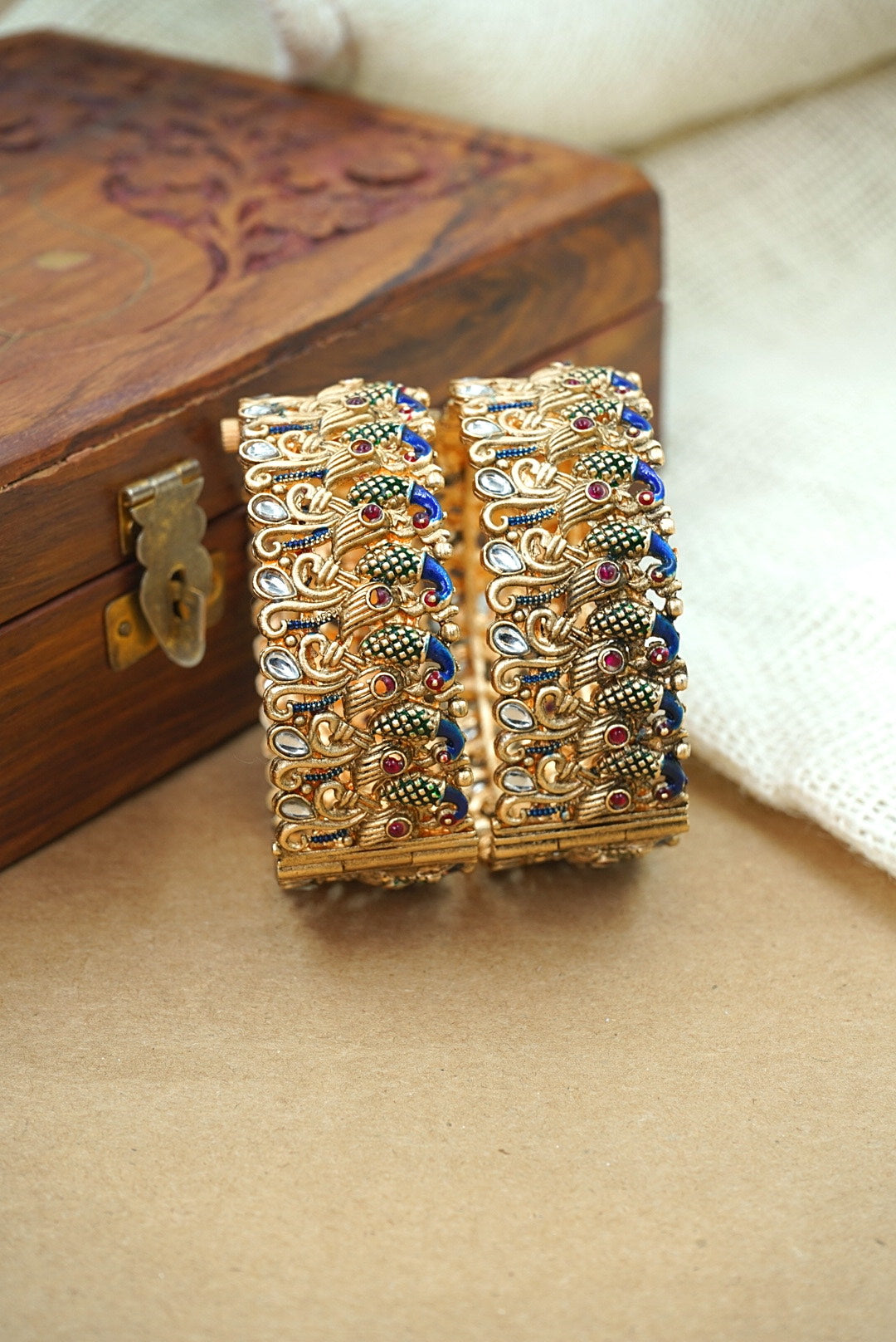 Pair of ornate gold bangles with gemstones on a wooden box by hitesh bangles