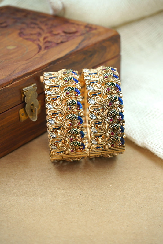 Pair of ornate gold bangles with gemstones on a wooden box by hitesh bangles