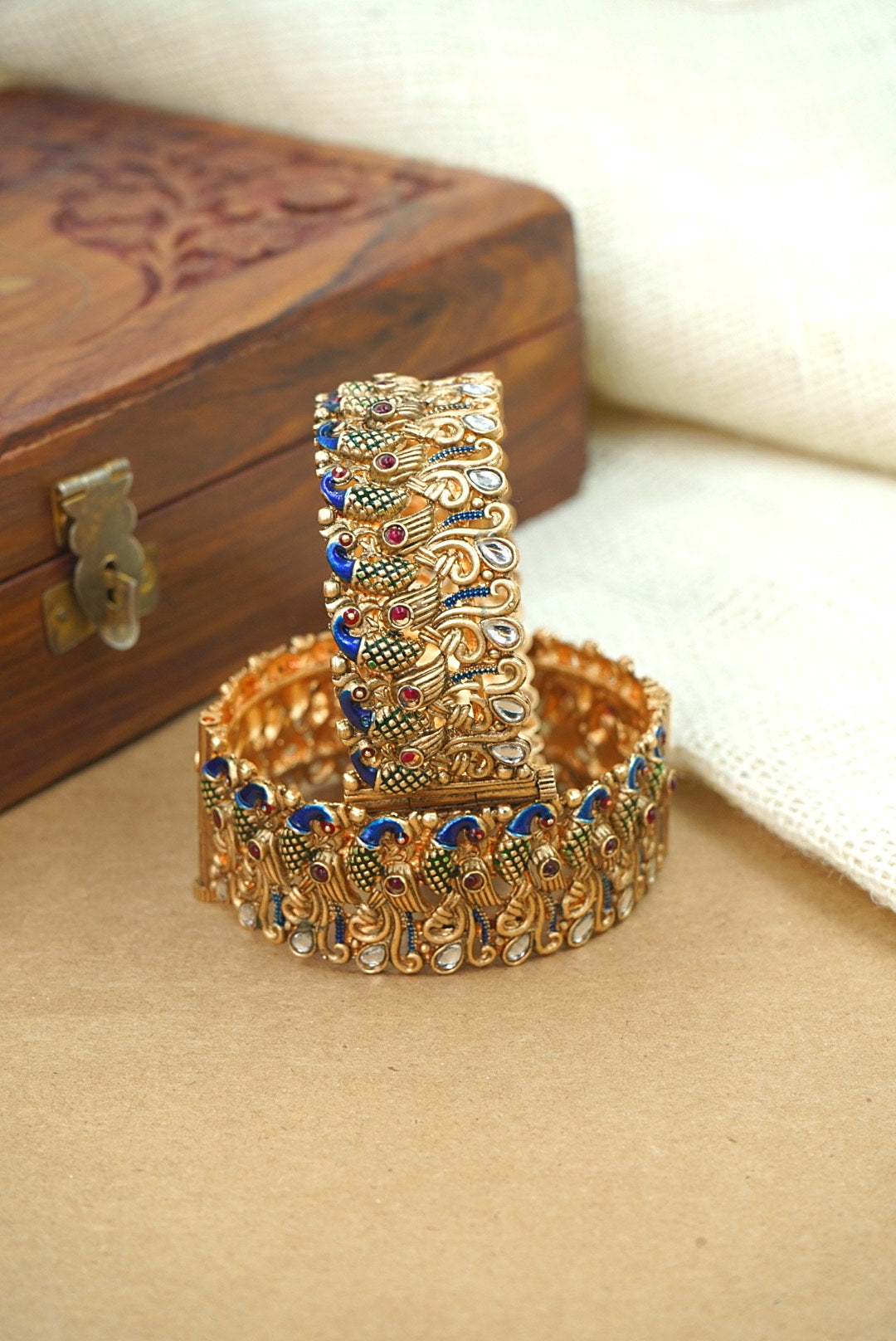 Decorative gold bangles with gemstones on a beige surface by hitesh bangles
