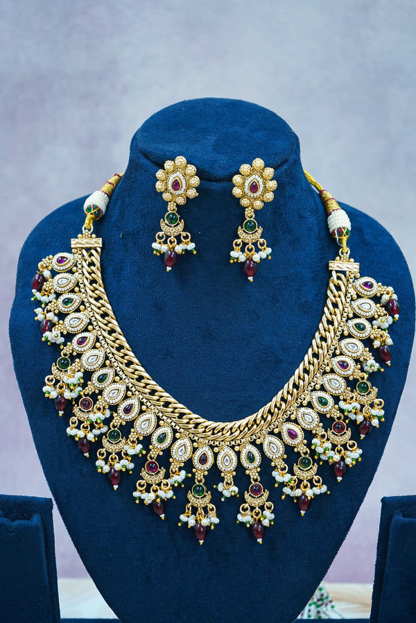 Gold necklace and earrings set on a blue stand with a gray background by hitesh bangles