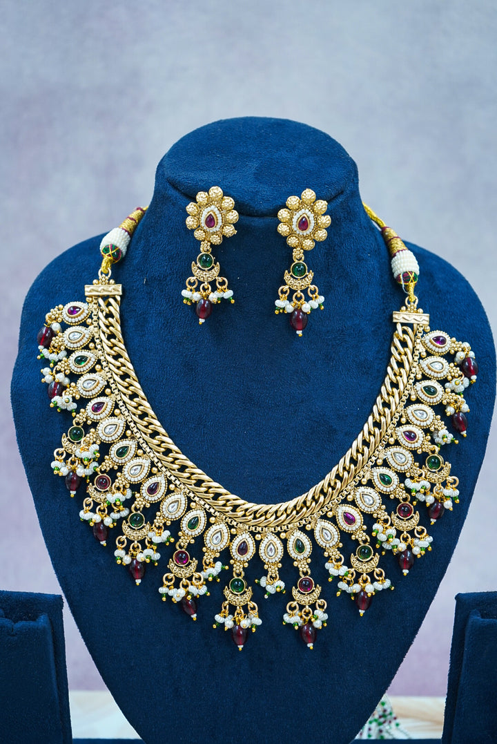 Gold necklace and earrings set on a blue stand with a gray background by hitesh bangles