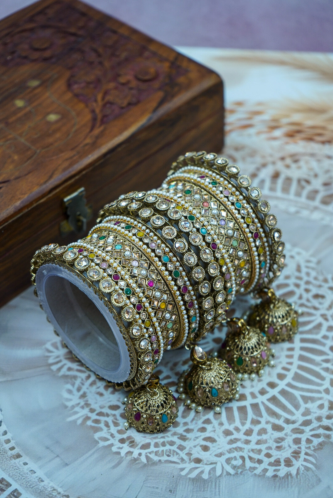 Decorative bangles with jhumkas on a lace tablecloth with a wooden box in the background by hitesh bangles