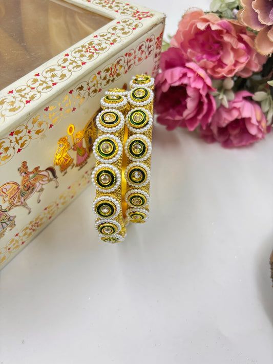 Decorative gold and green bangles with a jewelry box and flowers in the background by hitesh bangles