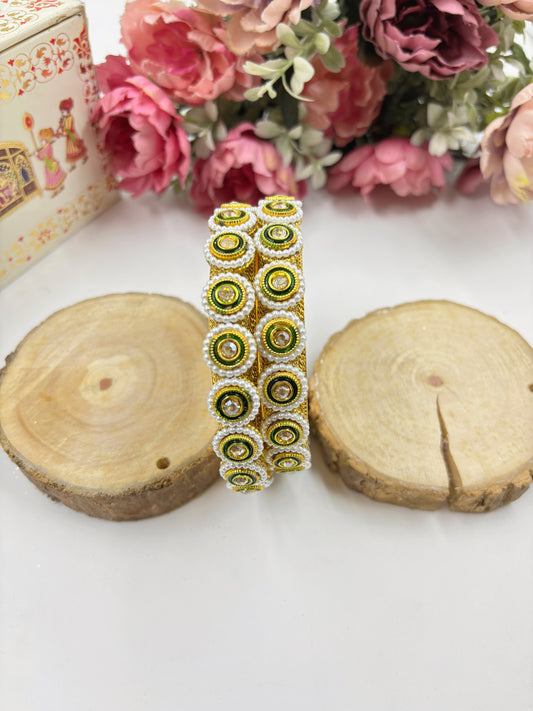 Decorative bracelet with green and gold pattern on a white surface with floral background by hitesh bangles