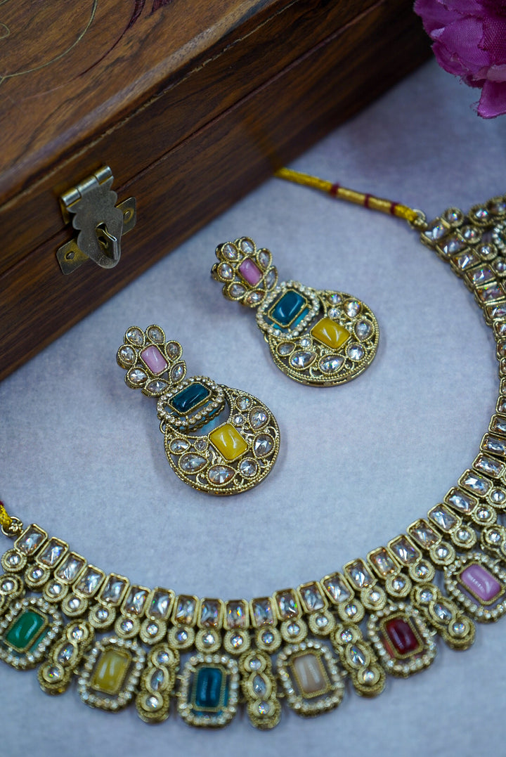 Gold necklace with colorful gemstones and matching earrings on a light gray surface by hitesh bangles