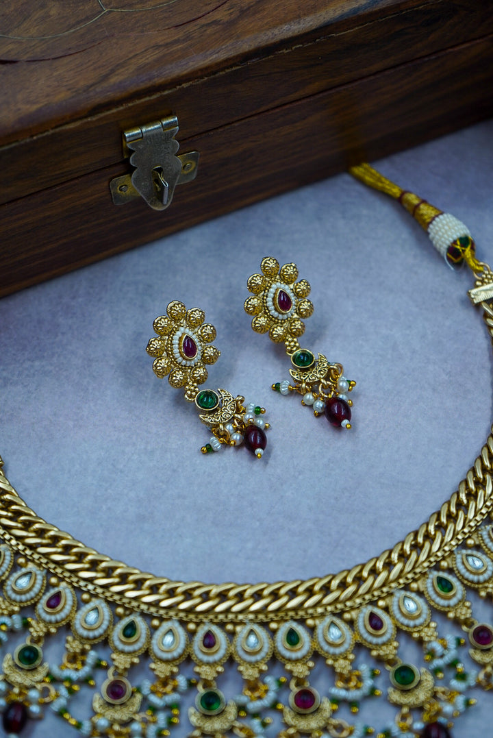 Gold necklace and earrings on a light blue surface with a wooden box in the background by hitesh bangles