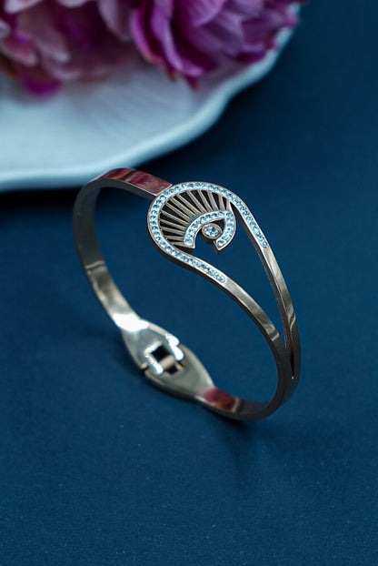 Silver bracelet with decorative elements on a blue surface with pink flowers in the background by hitesh bangles