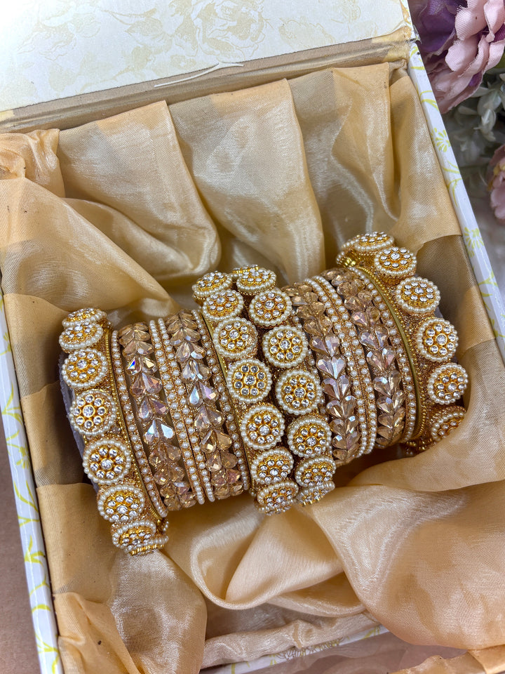 Golden bridal chooda set featuring intricate stone-studded circular kadas and shimmering crystal bead bangles, displayed with floral décor and a decorative box