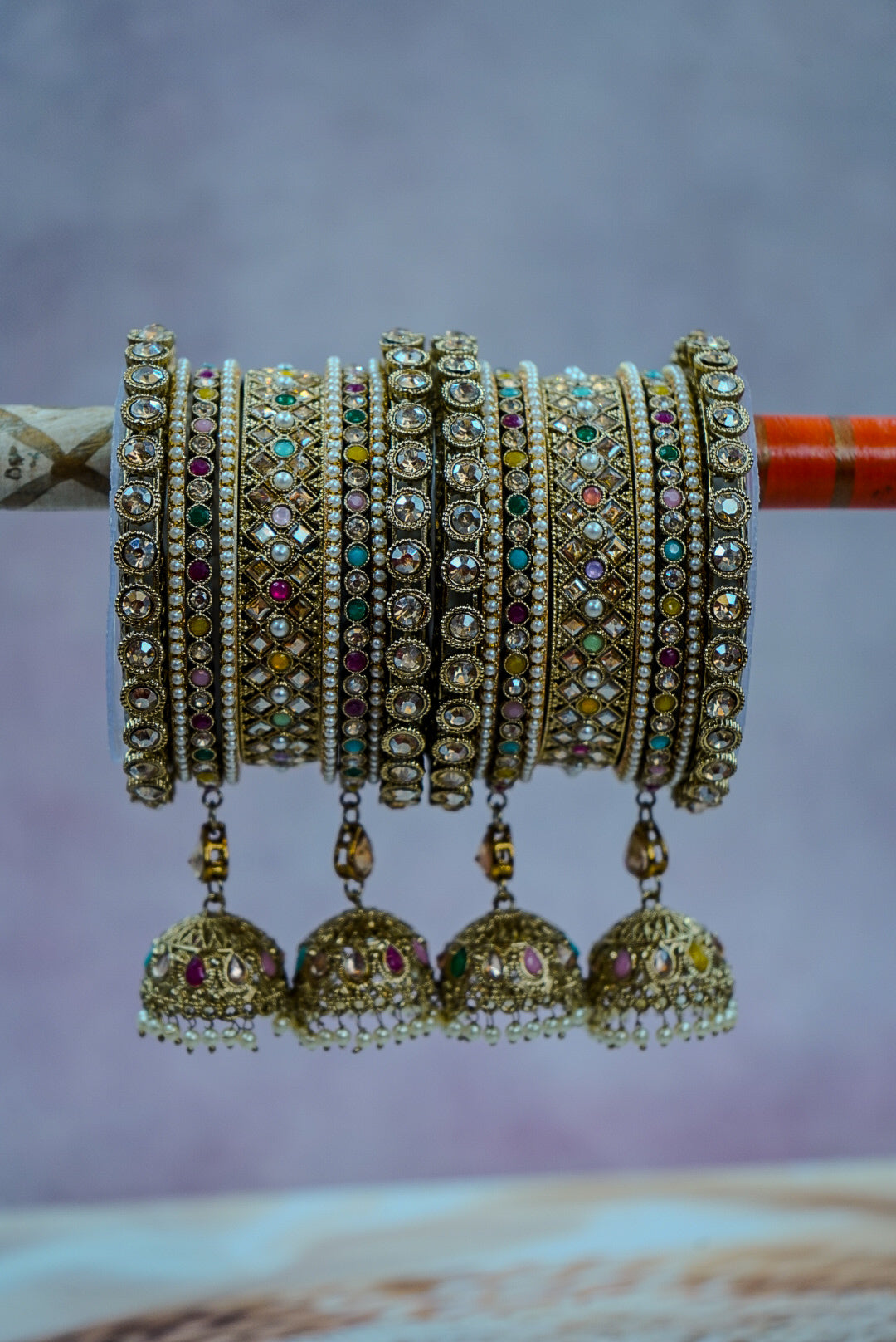 Set of gold jewelry with intricate designs and colorful stones on a purple background by hitesh bangles