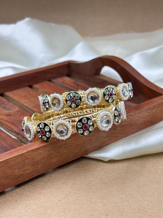 Pair of gold and silver bangles with red stones on a wooden stand by hitesh bangles