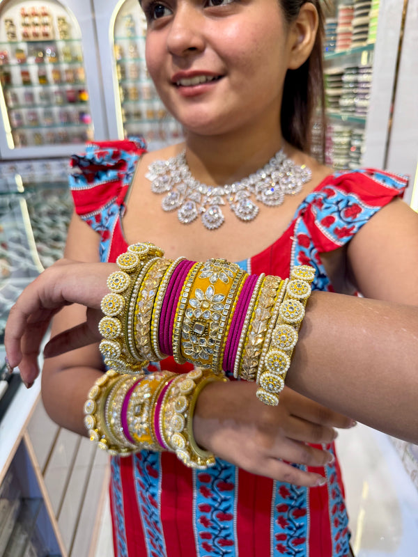 Bridal chura set featuring vibrant yellow and pink velvet bangles, embellished with intricate kundan, pearl, and gold-toned stonework, worn on both hands with detailed craftsmanship on display in a jewelry showroom.