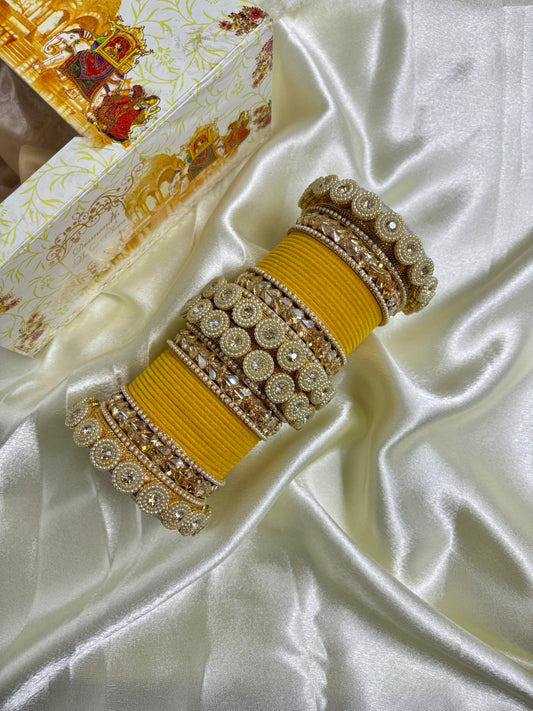 Decorative yellow bangles with intricate gold patterns on a white fabric background by hitesh bangles