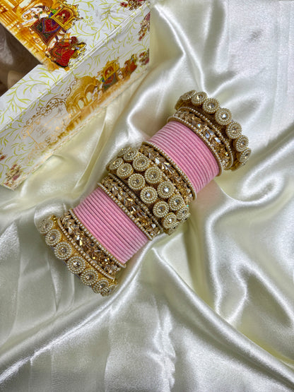 Decorative pink and gold bangles on a white satin surface with a decorative box in the background by hitesh bangles