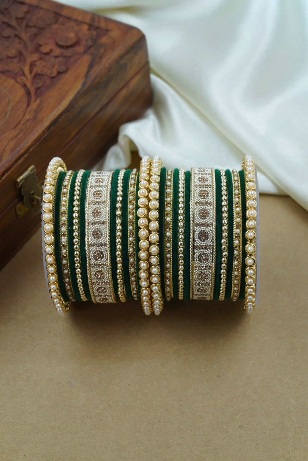 Set of green and gold bangles on a brown surface with a white fabric and wooden box in the background by hitesh bangles