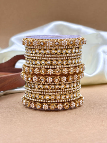 Stack of gold and pearl bangles on a beige surface with a white container in the background by hitesh bangles