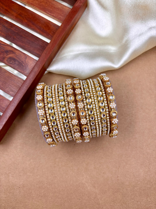 Set of gold bangles with intricate designs on a beige surface by hitesh bangles