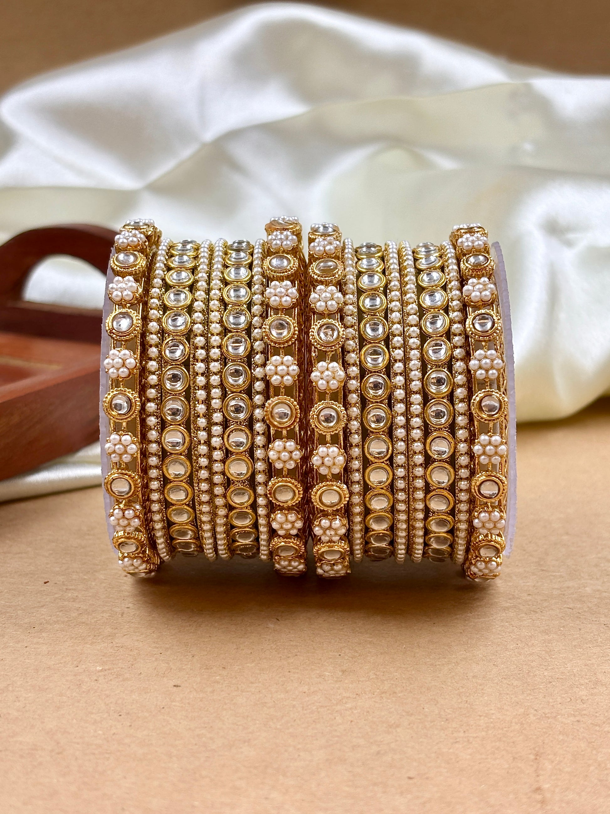 Set of gold and white beaded bangles on a beige surface with a white fabric background by hitesh bangles