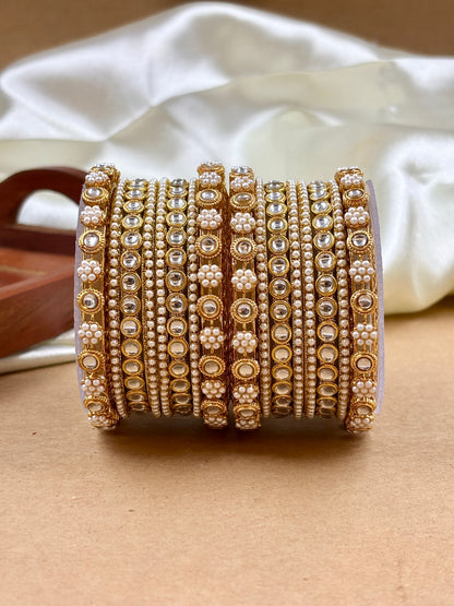 Set of gold and white beaded bangles on a beige surface with a white fabric background by hitesh bangles