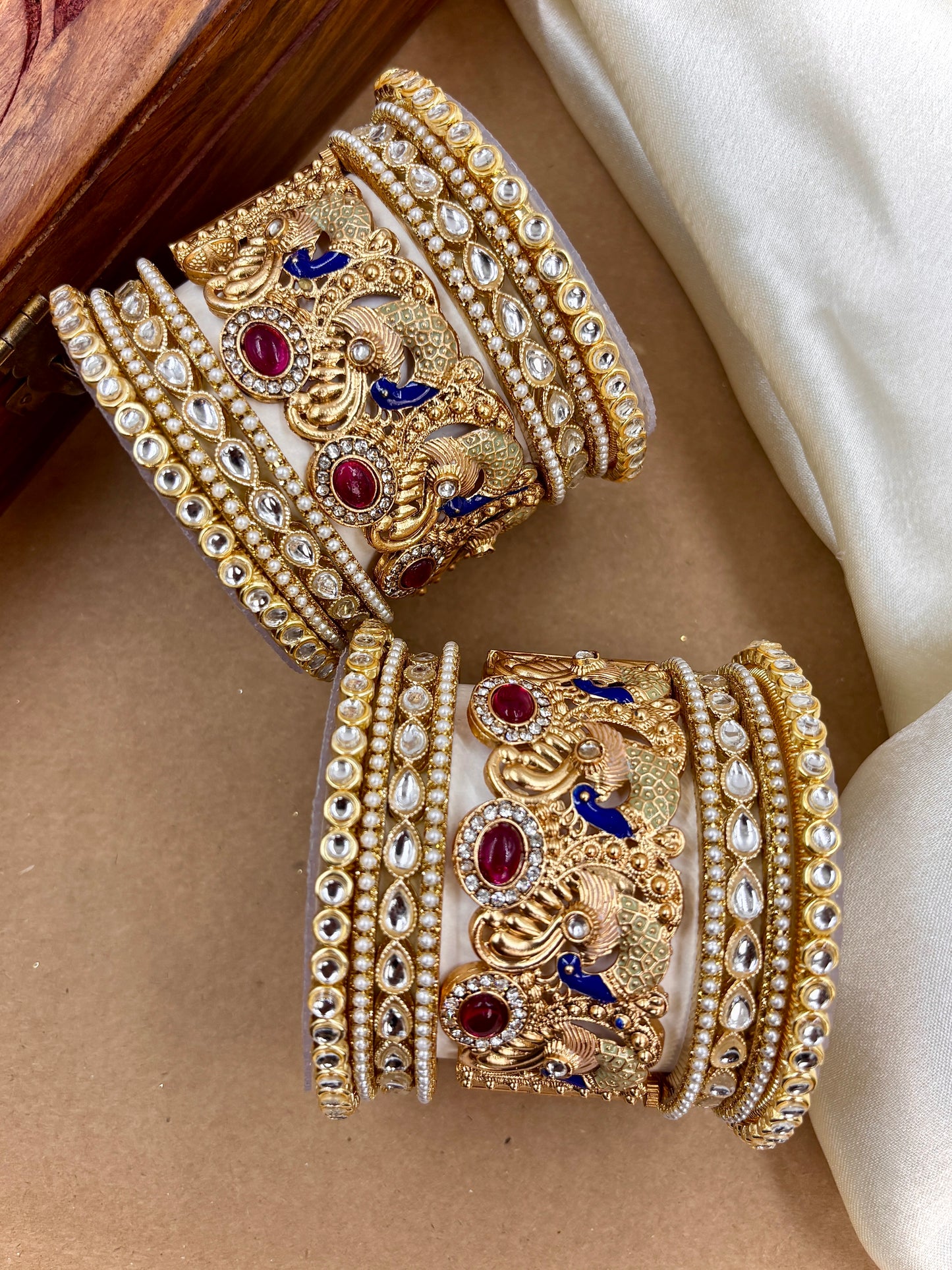Pair of ornate gold bangles with gemstones on a beige surface by hitesh bangles