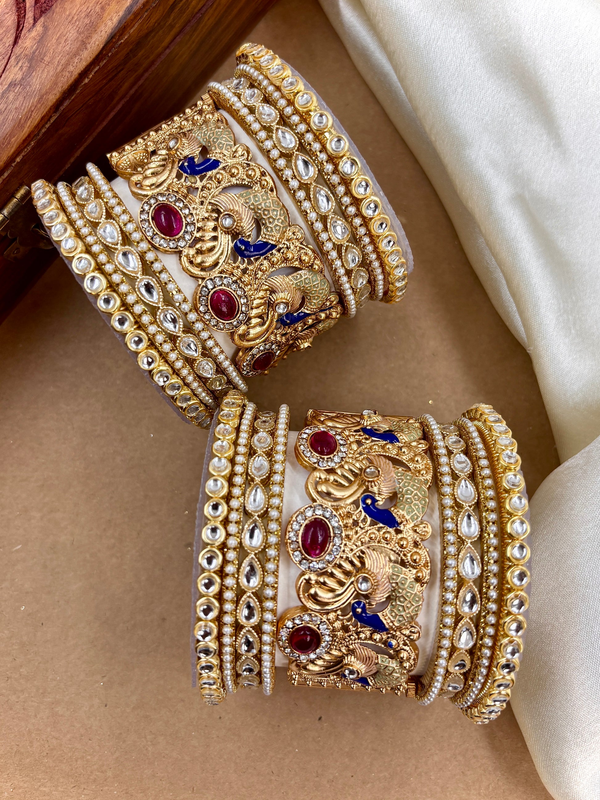 Pair of ornate gold bangles with gemstones on a beige surface by hitesh bangles