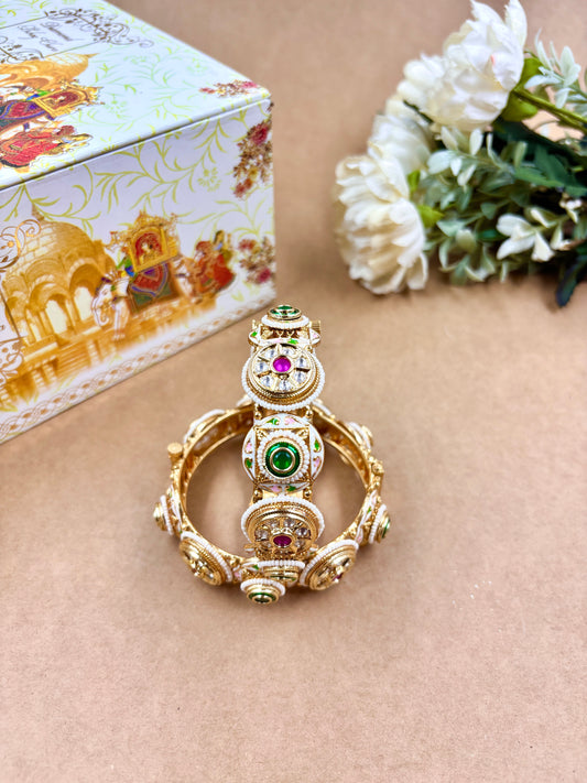 Decorative ring with gemstones on a beige surface, next to a decorative box and white flowers by hitesh bangles