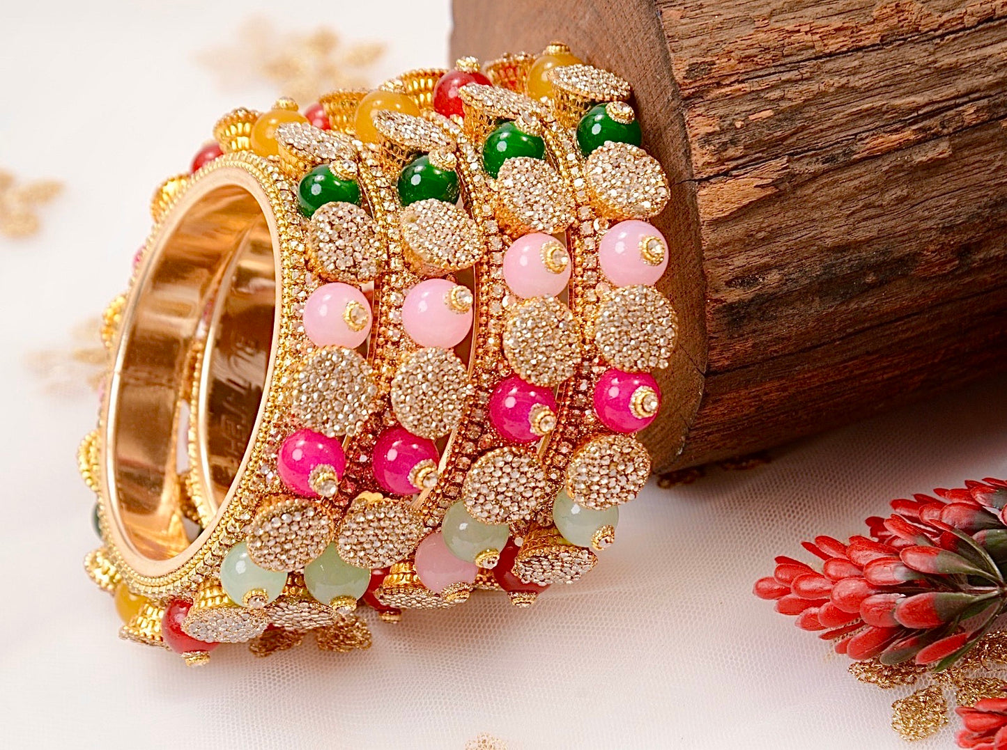 Decorative bangles with gold, green, pink, and red beads on a wooden surface by hitesh bangles