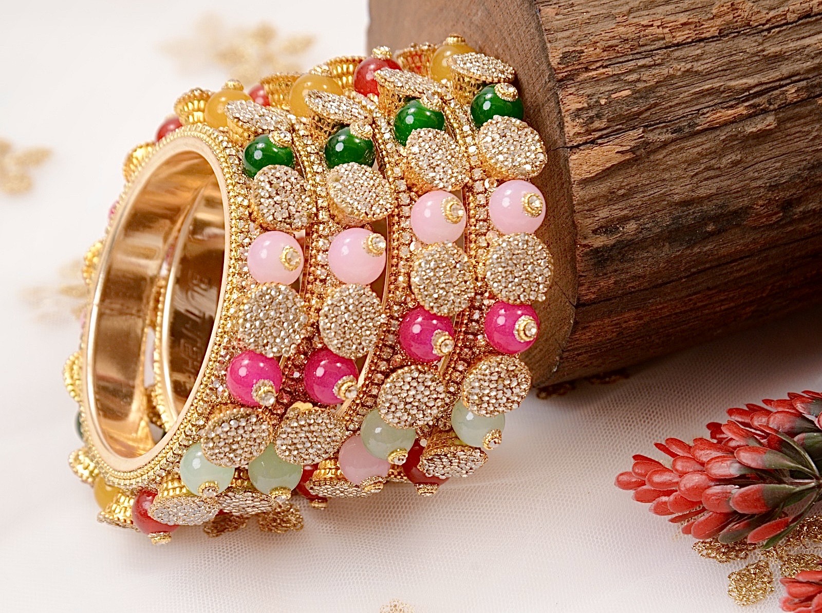 Decorative bangles with gold, green, pink, and red beads on a wooden surface by hitesh bangles