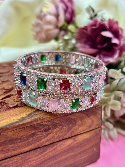 Silver bracelet with colorful gemstones on a wooden surface with flowers in the background by hitesh bangles
