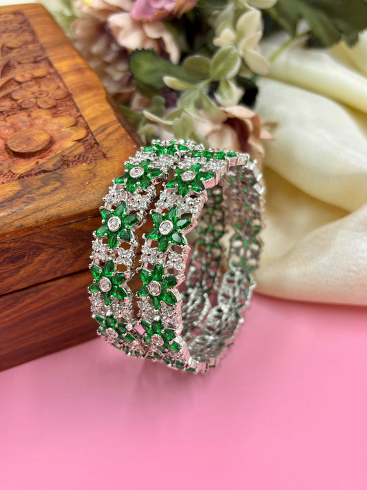 Decorative bracelet with green and clear stones on a pink surface with floral background by hitesh bangles