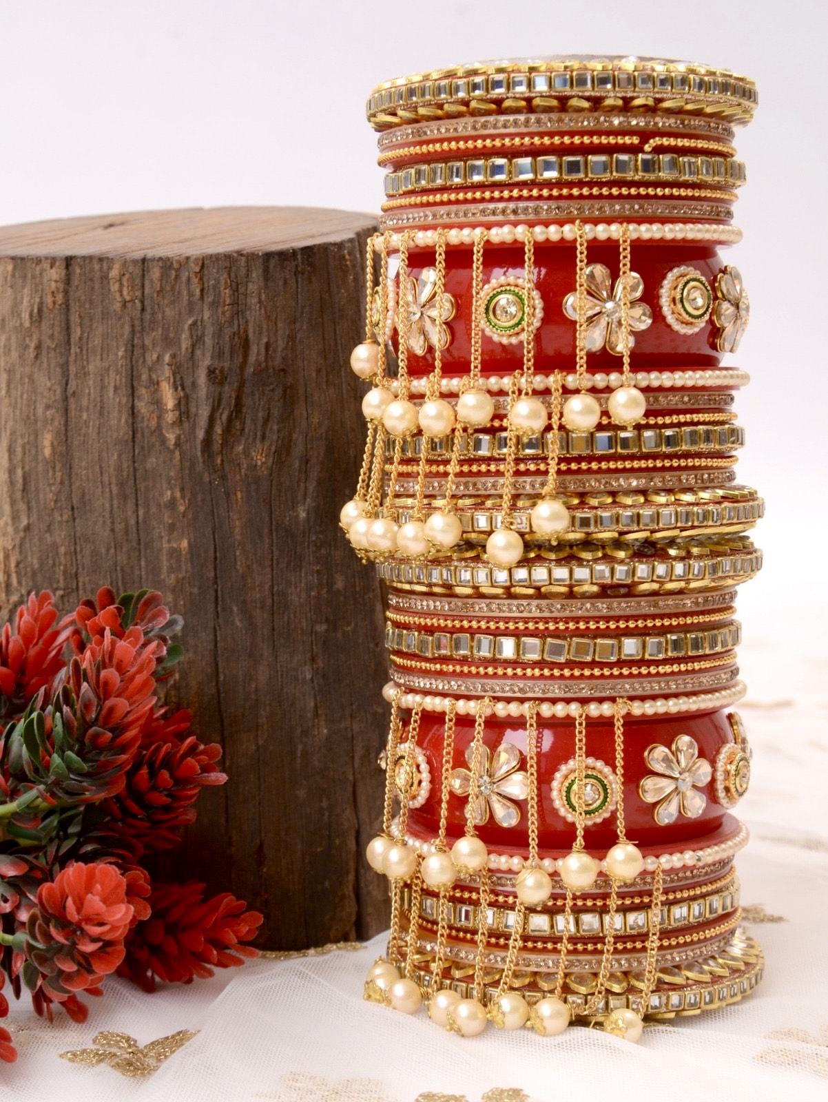 Stack of ornate bangles on a red cylindrical stand with floral decorations by hitesh bangles