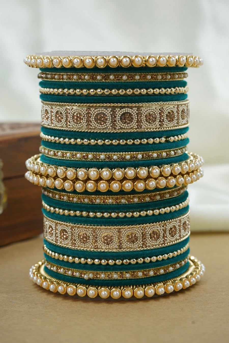 Stack of decorative bangles with pearls and patterns on a neutral background by hitesh bangles