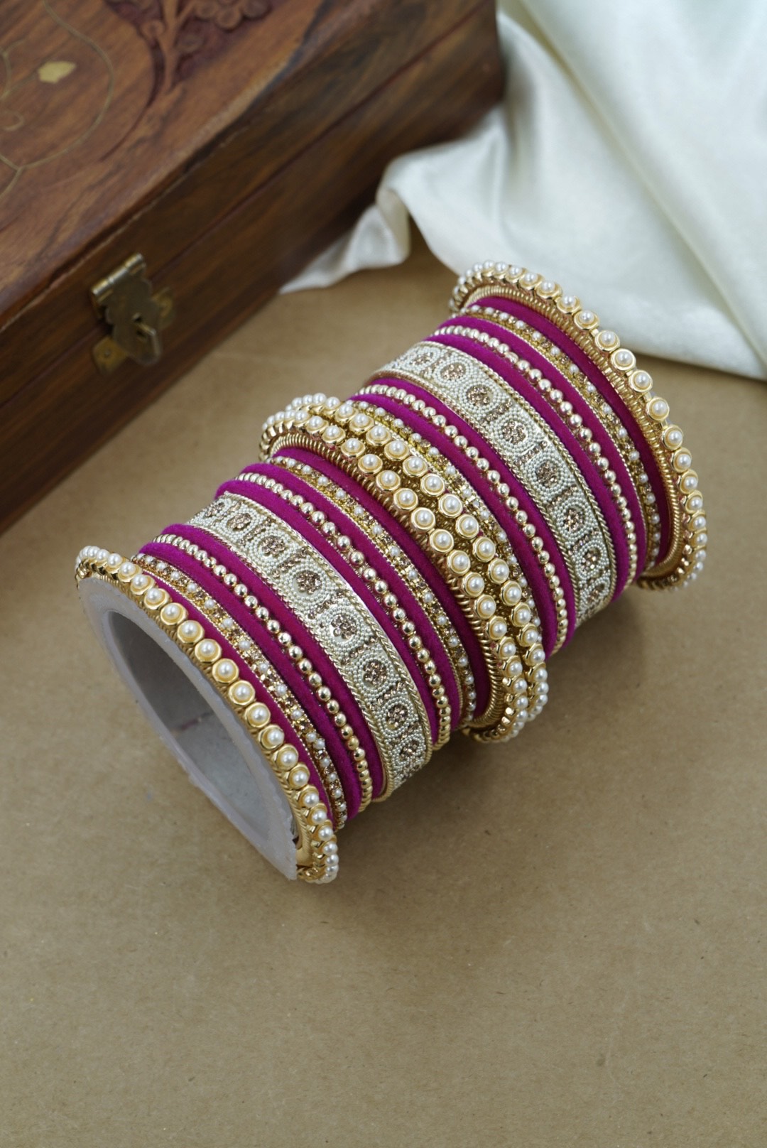 Set of purple and gold bangles on a beige surface with a wooden box in the background by hitesh bangles