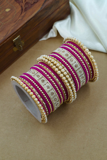 Set of purple and gold bangles on a beige surface with a wooden box in the background by hitesh bangles