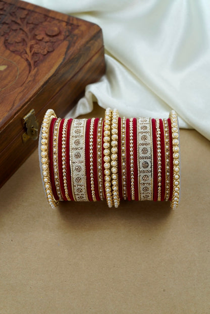 Set of red and gold bangles on a beige surface with a white fabric and wooden box in the background by hitesh bangles